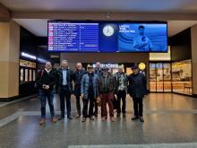 La délégation FTJA tout sourire devant le panneaux des horaires. "Que la ligne Berne-Neuchâtel-Travers-Pontarlier-Frasne-Paris libère son potentiel!" semble suggérer la publicité